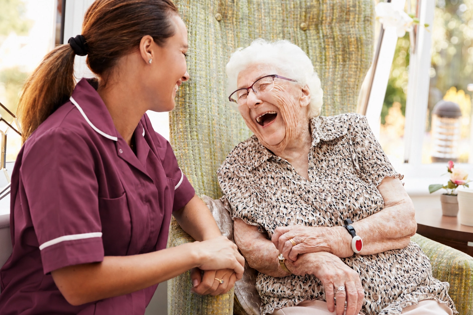 lauging senior sat on a cozy chair with caregiver